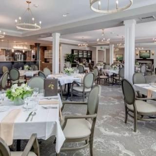 An elegant restaurant interior with well-arranged dining tables and chairs, adorned with fresh floral centerpieces and ambient lighting from chandeliers.