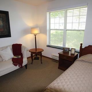 A cozy bedroom featuring a bed, sofa, and standing lamp by the window.