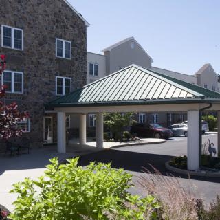 A residential building with a stone facade featuring a covered entrance and landscaped surroundings.