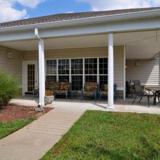 A cozy patio with seating in a garden setting, featuring columns and a house exterior.
