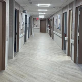A long hospital corridor with multiple doors and bright fluorescent lighting.