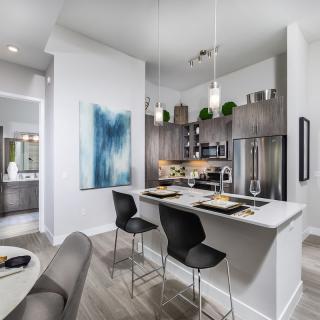 A modern kitchen with a sleek design featuring a dining area, pendant lights, and contemporary artwork.