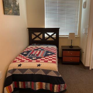 A cozy single bedroom featuring a patterned quilt and a bedside lamp.