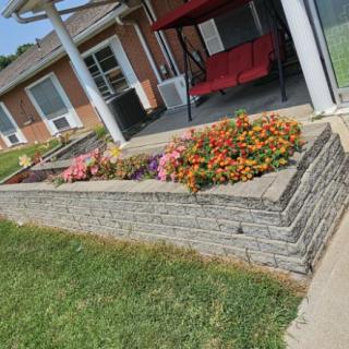 A well-maintained flower bed with colorful blooms bordered by a brick wall, adjacent to a patio area with a swing bench.