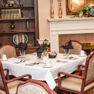 An elegantly set dining table in a formal dining room with a fireplace and bookshelf in the background.
