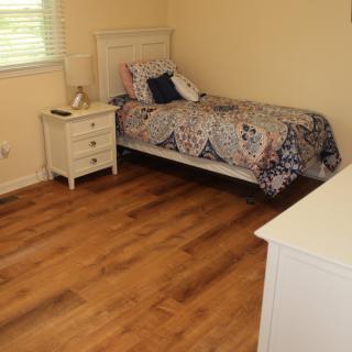 A simple bedroom with a single bed, nightstand, and dresser on wooden flooring.