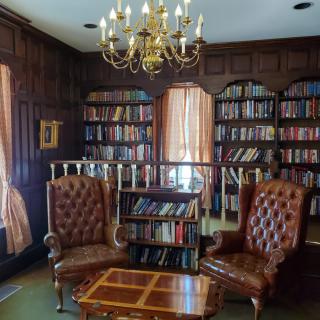A cozy library with leather chairs and wooden bookshelves under a chandelier.