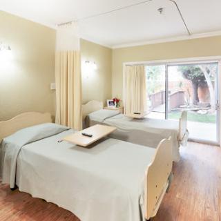 A spacious hospital room featuring two beds with warm lighting and a view of the outdoor area.