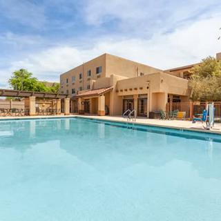 An outdoor swimming pool adjacent to a hotel building under a clear blue sky.
