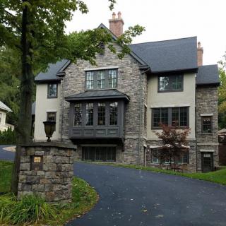 A large stone house with a curved driveway and surrounding trees.