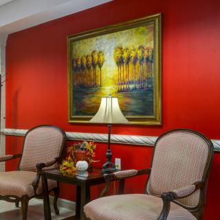A cozy sitting area with two chairs, a table, and a lamp against a vibrant red wall adorned with a colorful painting.