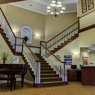 A spacious lobby featuring a grand staircase, chandelier, and a piano.