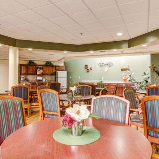 A communal dining area with multiple tables and chairs, featuring a small kitchen section in the background.