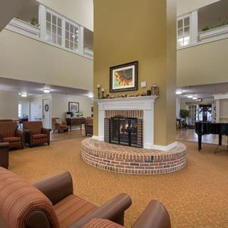 A cozy living room with a central fireplace, comfortable seating, and a grand piano in the background.