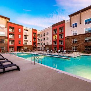 A modern apartment complex featuring a large outdoor swimming pool surrounded by lounge chairs.