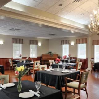 An elegant dining room with neatly set tables and chairs, featuring a chandelier and tasteful decor.