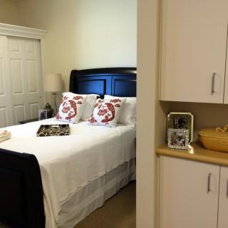 A cozy bedroom with a neatly made bed, decorative pillows, and a nightstand featuring a lamp and photo frame.