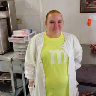 A person wearing a bright yellow shirt and a white coat in a kitchen setting.