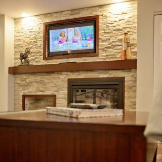 A cozy living room with a stone fireplace and a television mounted above the mantel.