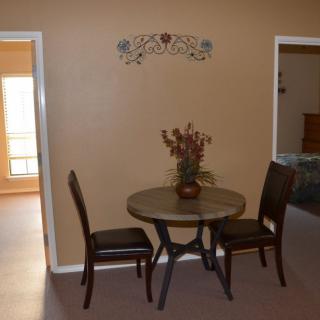 A small dining area with a round table and two chairs, decorated with wall art and a vase of flowers.