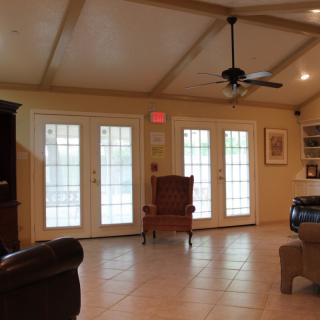 A spacious living room with large windows, an armchair, and a ceiling fan.