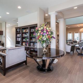 A modern living room with elegant decor, featuring a central table with a floral arrangement and a bookshelf in the background.