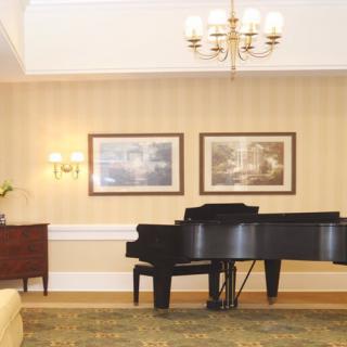 A cozy living room featuring a grand piano under a chandelier, with framed art on the wall.