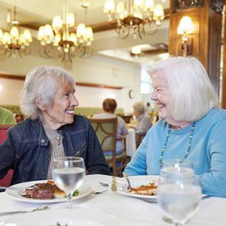 Two elderly women enjoy a meal and conversation in a restaurant.