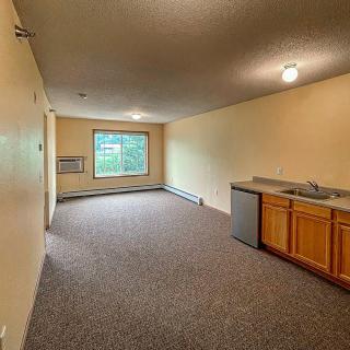 An empty room with a kitchenette and large window.