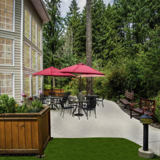A cozy outdoor patio with tables, chairs, and red umbrellas surrounded by lush greenery.