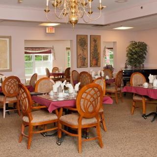 A cozy dining room setup with elegantly decorated tables and wooden chairs, featuring a chandelier hanging from the ceiling.