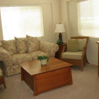 A cozy living room featuring a patterned sofa, wooden coffee table, armchair, and a lamp by the window.
