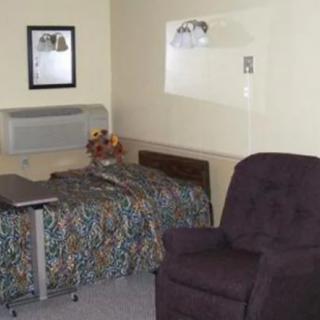 A small hotel room featuring a single bed, an armchair, and a framed picture on the wall.