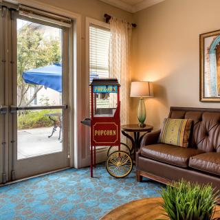 A cozy living room featuring a vintage popcorn machine, leather sofa, and soft lighting from a lamp near a window with a view outside.