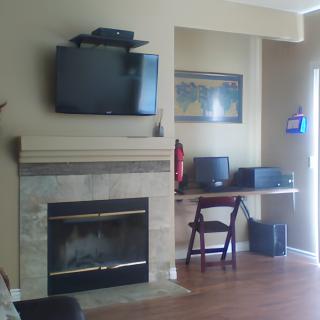 A cozy living room featuring a fireplace and mounted TV, with a nearby desk and chair setup.