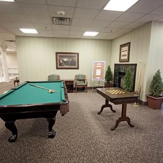 A cozy game room featuring a pool table and chess board set, complete with comfortable chairs and decorative elements.
