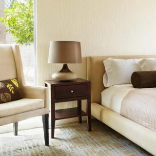 A cozy bedroom with a neutral color palette, featuring a comfortable chair, a nightstand with a lamp, and a neatly made bed.