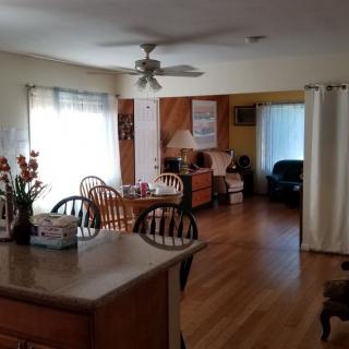 A cozy dining and living area with wooden flooring, natural lighting, and comfortable furnishings.