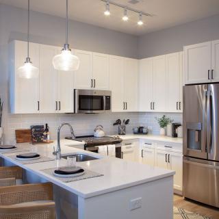 A modern kitchen with white cabinets and a central island, featuring stainless steel appliances and stylish pendant lighting.