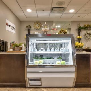 A modern cafe interior featuring a dessert display case surrounded by decorative flowers.