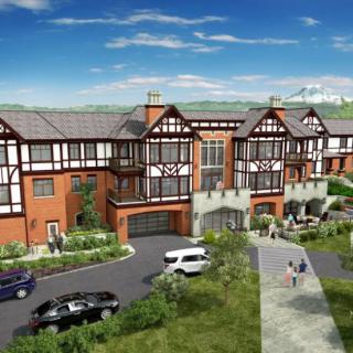 A Tudor-style residential building surrounded by landscaping, with parked cars and people walking along a pathway under a clear blue sky.