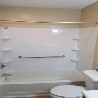 A modern bathroom featuring a combined bathtub and shower with shelving, along with a toilet.