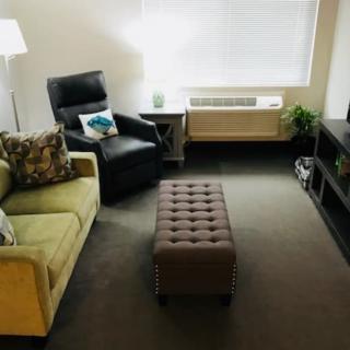 A cozy living room with a sofa, armchair, ottoman, and a lamp.