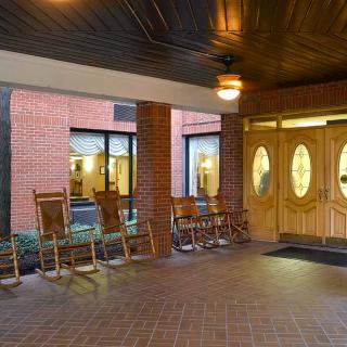 A cozy entrance area with rocking chairs lined up against a brick wall, facing glass doors under a wooden ceiling.