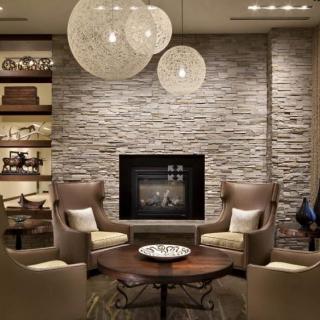 A cozy modern living room with a stone wall and fireplace, featuring a seating area with armchairs and hanging pendant lights.