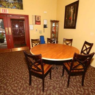 A small conference room featuring a round wooden table surrounded by four chairs, with artwork on the walls and a carpeted floor.