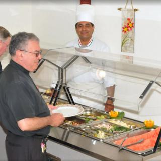A person serving themselves at a buffet with a chef overseeing the food display.