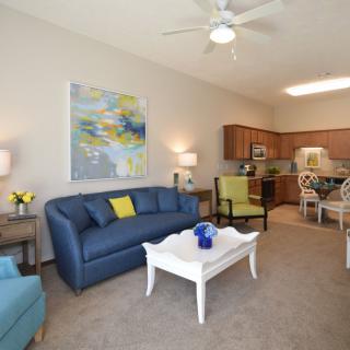 A modern living room with a blue sofa, white coffee table, and an open kitchen dining area.