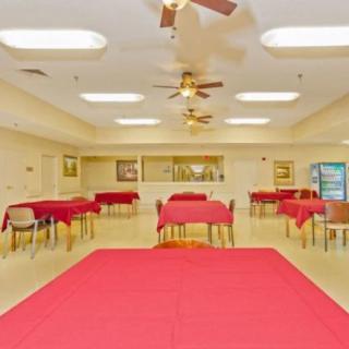 An indoor dining area with red tablecloths, tables and chairs, bright lighting, and ceiling fans.