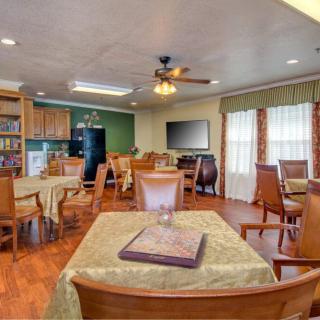 A cozy dining area with wooden tables and chairs, featuring a kitchen in the background.